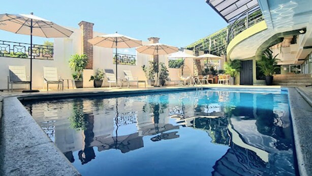 Una piscina amb gandules i ombrel·les, envoltada de plantes en testos i una estructura d'edifici modern.