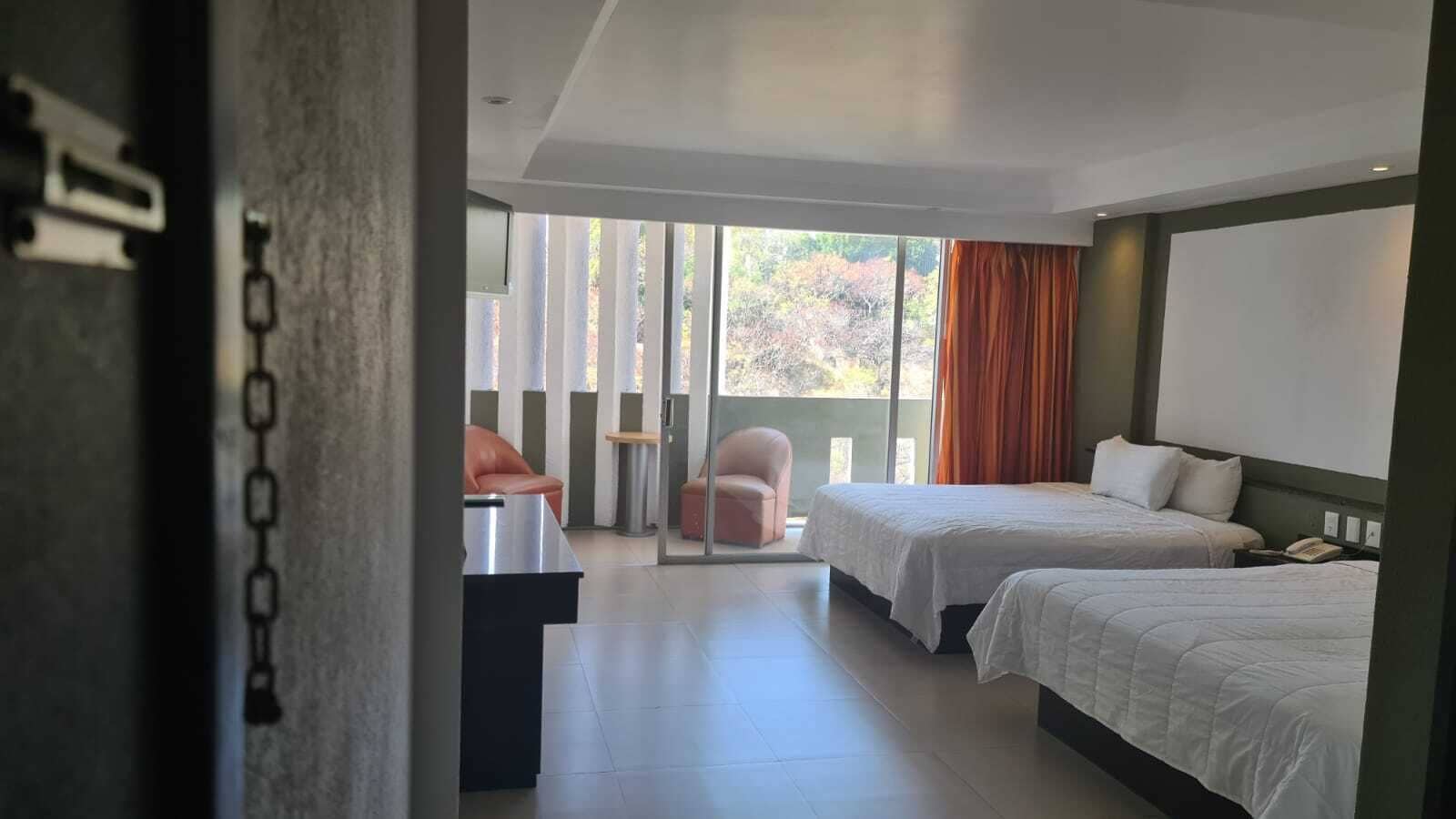 A hotel room with two beds, a desk, a chair, and a view of the outdoors.