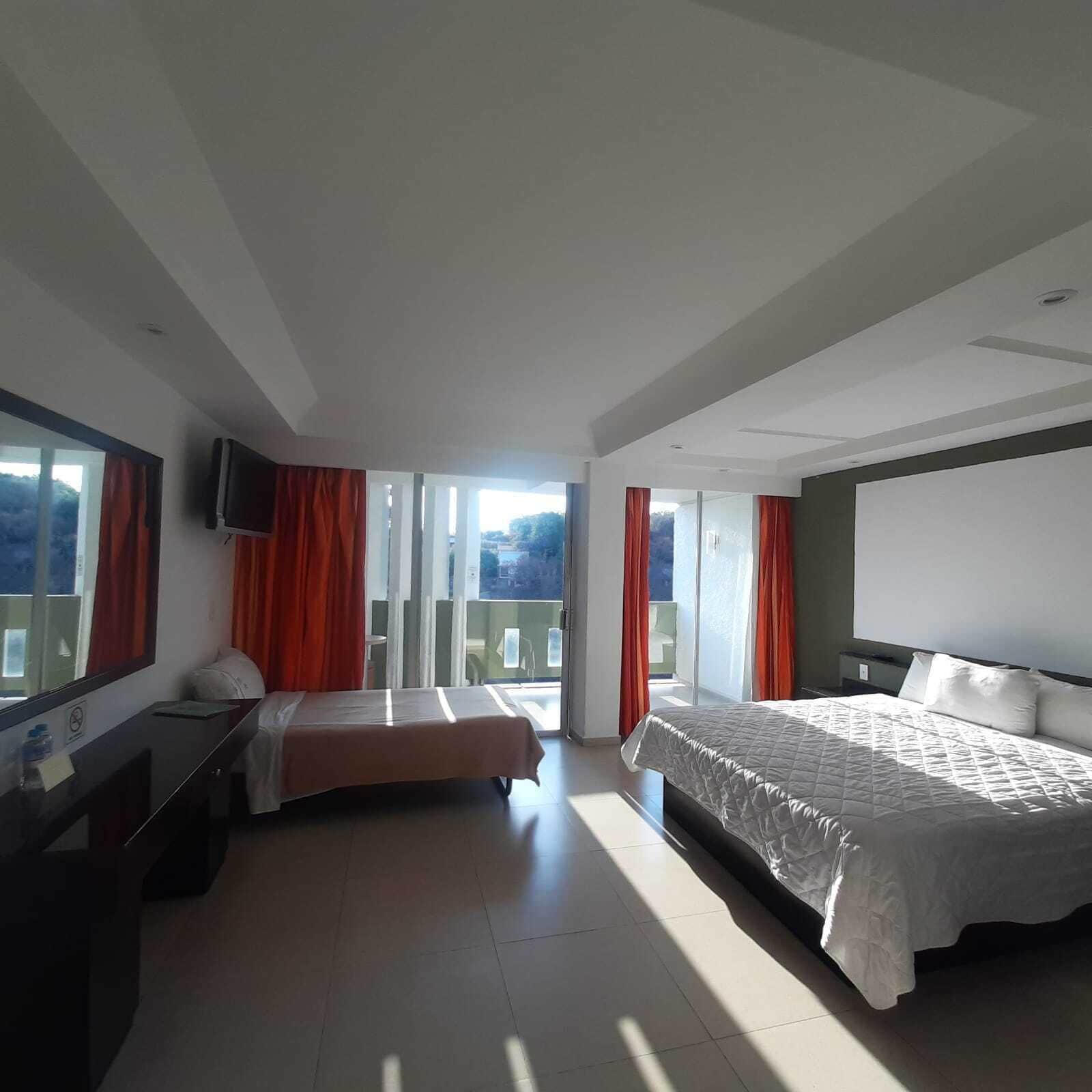 A hotel room with a bed, a desk, a TV, and a balcony with red curtains.