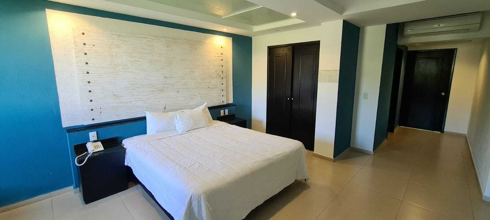 Habitación de hotel con una cama grande, una mesita de noche con teléfono, una lámpara de pared y dos puertas.