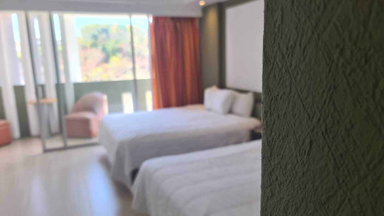 Habitación de hotel con dos camas, puerta corrediza de vidrio que da a un balcón y vista al exterior.