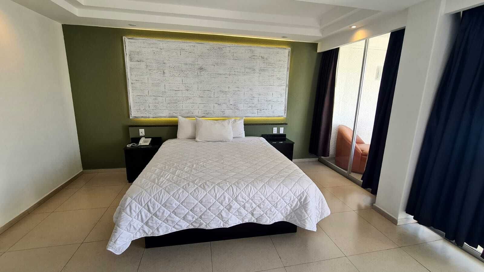 Ein Hotelzimmer mit einem großen Bett, einem Nachttisch, einem an der Wand befestigten Fernseher und einer Schiebeglasdoor.