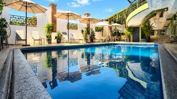 Una piscina al aire libre, sombrillas, sillones reclinables de piscina