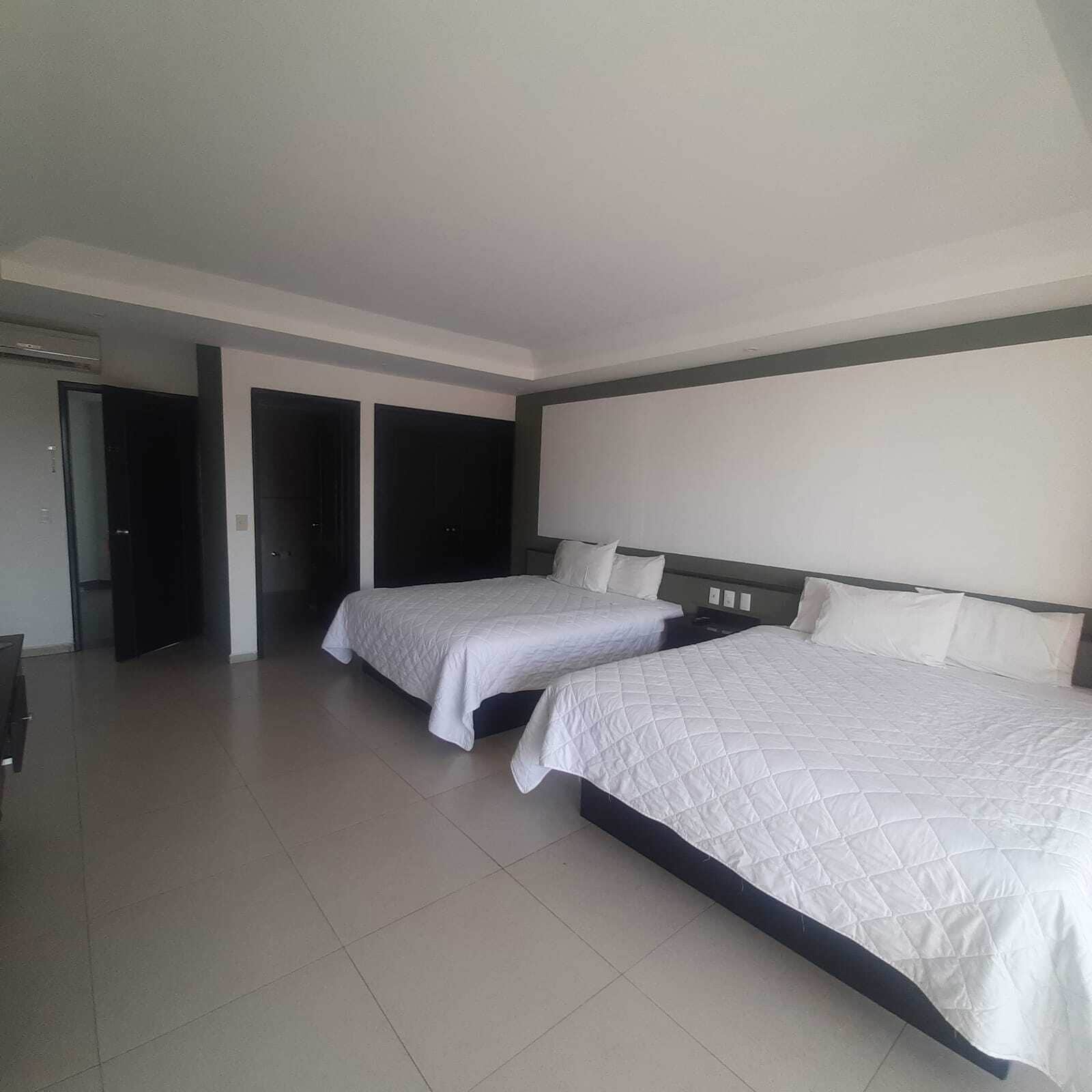 Una habitación de hotel con dos camas, un ventanal grande y una puerta que da a un pasillo.