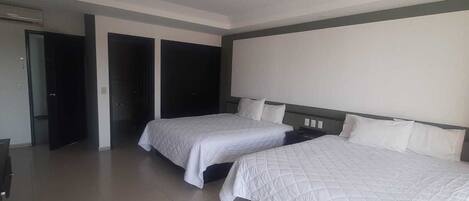 A hotel room with two beds, a large window, and a door leading to a hallway.
