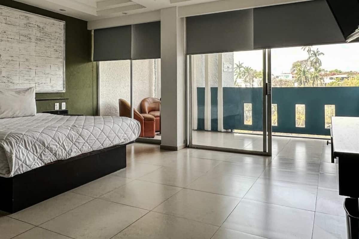 A hotel room with a bed, a chair, a desk, and a large window.