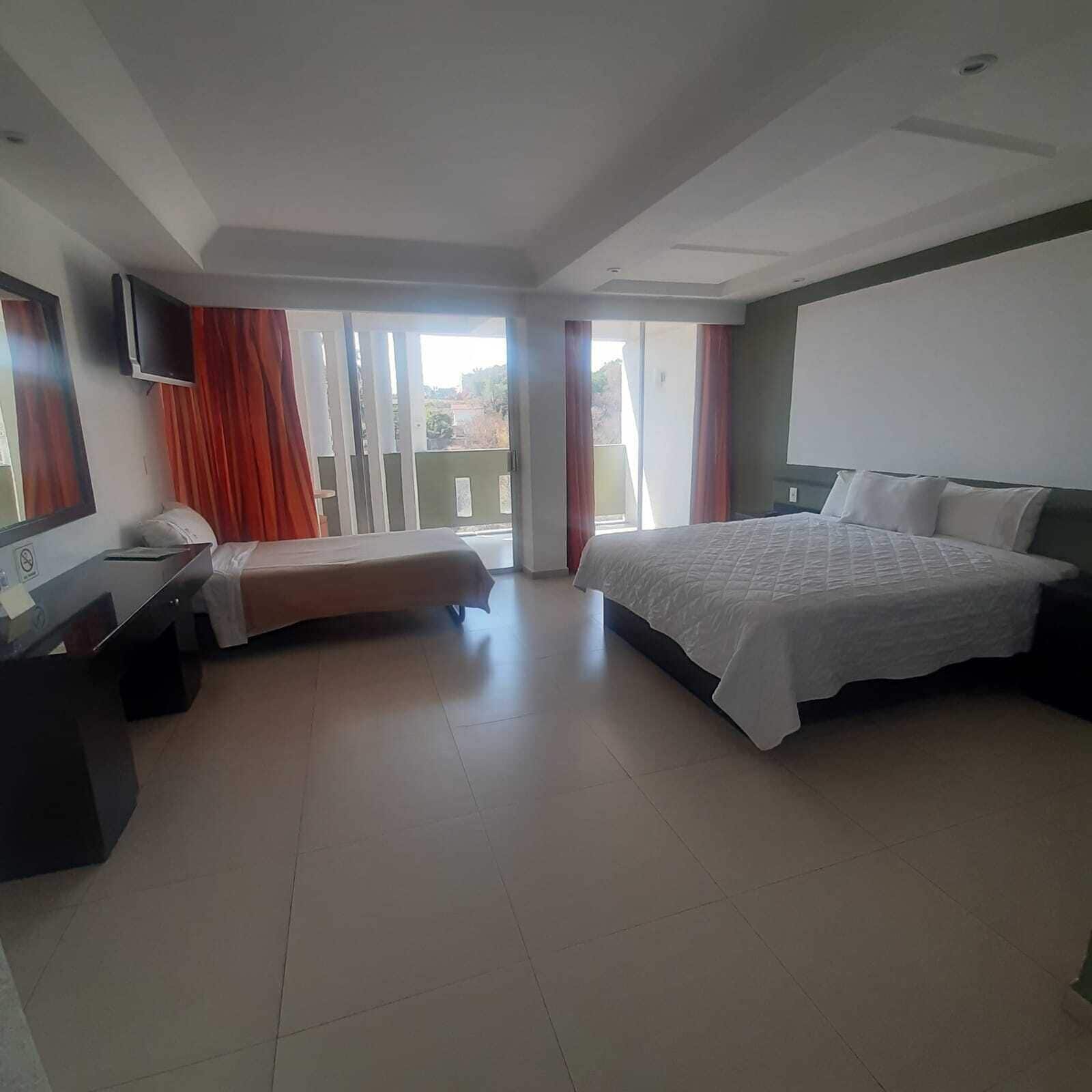 A hotel room with a bed, a desk, a TV, and a balcony with curtains.