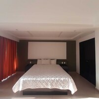 Un dormitorio moderno con una cama grande, un televisor de pantalla plana y un armario de color oscuro.