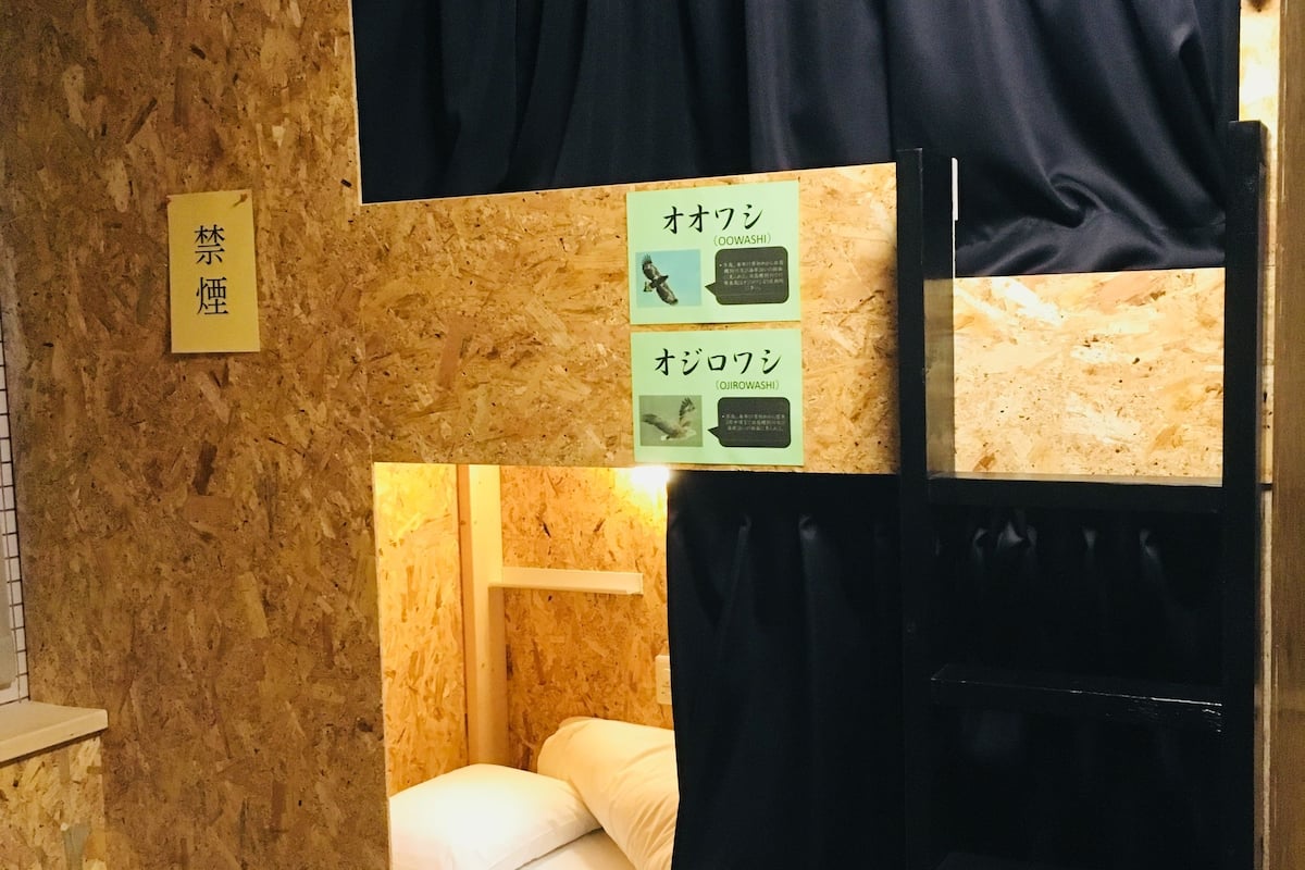 A bunk bed with a wooden wall and a small window. There are signs with Japanese text and images of birds.