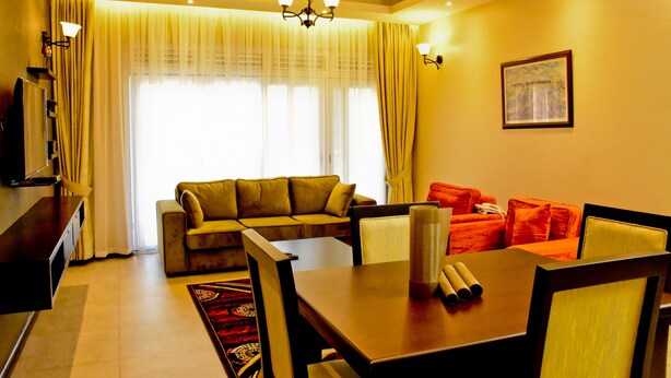 A living room with a sofa, a dining table with chairs, a TV, and a chandelier. - Greendale Apartments (Kampala)
