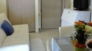 Um quarto com um sofá branco, uma mesa de jantar com cadeiras, uma TV em um móvel e uma porta fechada.