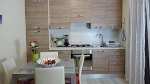 Cozinha compacta com armários de madeira, fogão a gás, pia e área de jantar com mesa e cadeiras.