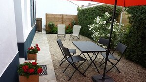 Un patio al aire libre con una mesa, sillas, un paraguas rojo y plantas en macetas.