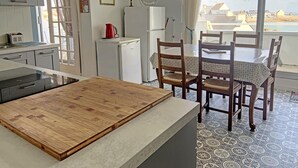 Une cuisine avec un plan de travail en bois, une table à manger avec des chaises, un réfrigérateur et une fenêtre donnant sur des bâtiments et une étendue d’eau.