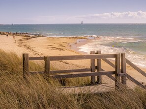 A beach with a wooden fence leading to the shore, grassy dunes, and the ocean.