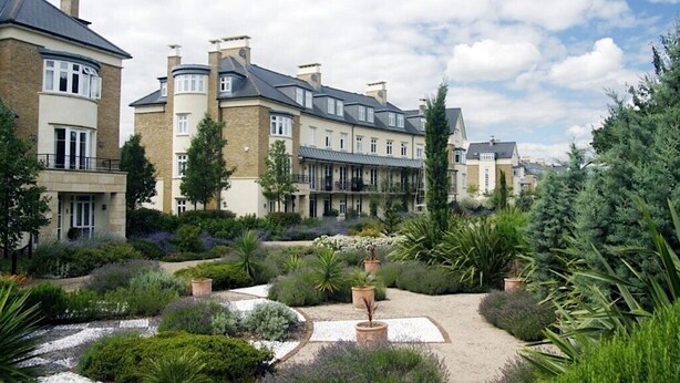 A residential building with multiple floors, large windows, and a garden with various plants and a gravel path. - King Size Bed in Large Room Kew Riverside Apartment  (Richmond)