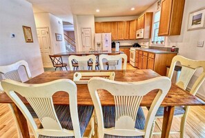 A dining area with a wooden table and white chairs, a kitchen with wooden cabinets, and a small island with a sink and stove.