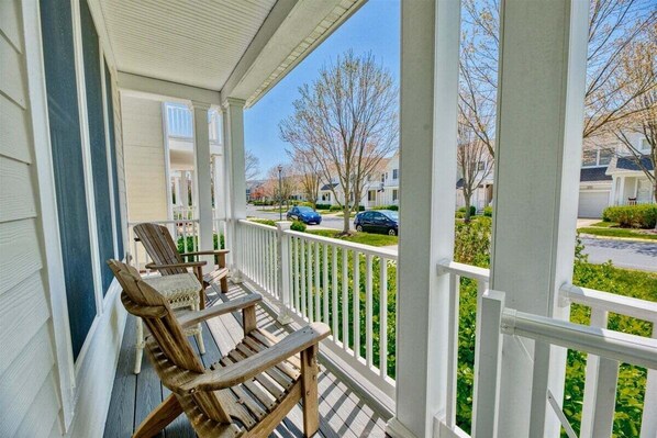 A porch with two wooden Adirondack chairs and a white railing.