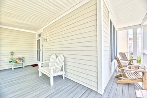 A covered porch with white wooden walls, a bench, and two Adirondack chairs.