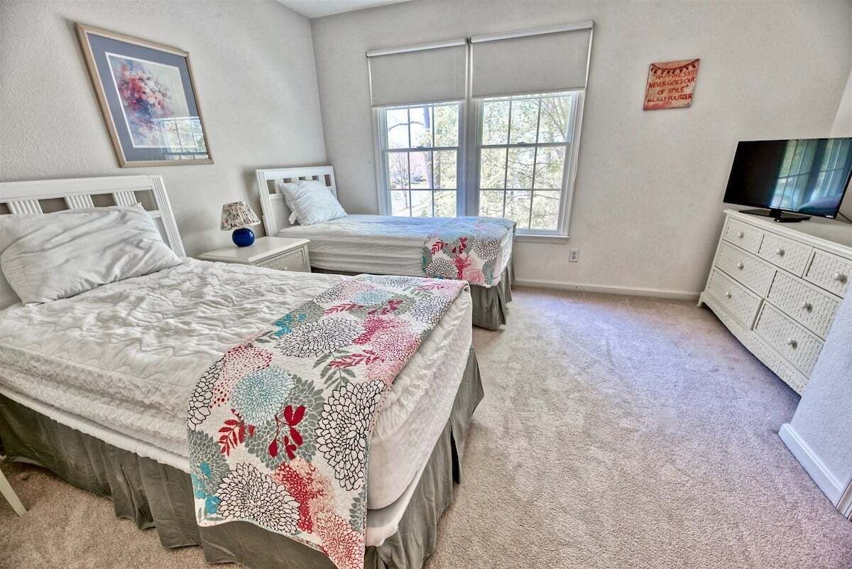 A bedroom with two beds, a TV, a dresser, and a window with blinds.