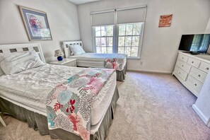 A bedroom with two beds, a TV, a dresser, and a window with blinds.