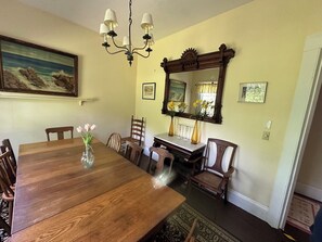 Una sala da pranzo con un tavolo in legno, sedie, un lampadario, uno specchio e un quadro appeso al muro.