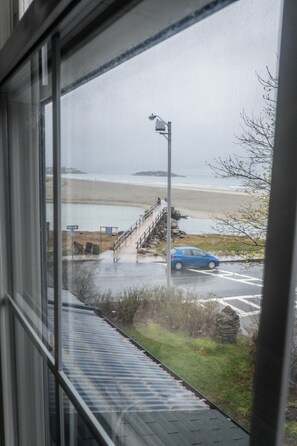 Vista dalla finestra su una spiaggia, con un'auto parcheggiata sulla strada.