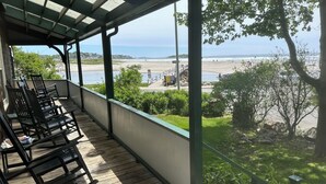 Un balcó cobert amb terres de fusta i cadires, amb vista a una platja i l'oceà.
