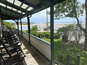 Un balcone coperto con pavimento in legno e sedie, con vista su una spiaggia e l'oceano.