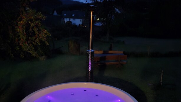 Een hottub met een houten terras, omringd door een gazon en een boom.