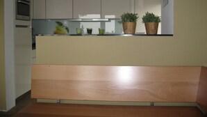 Una cocina con armarios blancos, un banco de madera y dos plantas en macetas sobre la encimera.