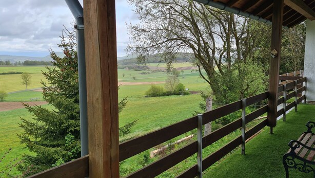 Un espacio al aire libre cubierto con cerca de madera, un banco y vistas a un paisaje verde con árboles y campos.