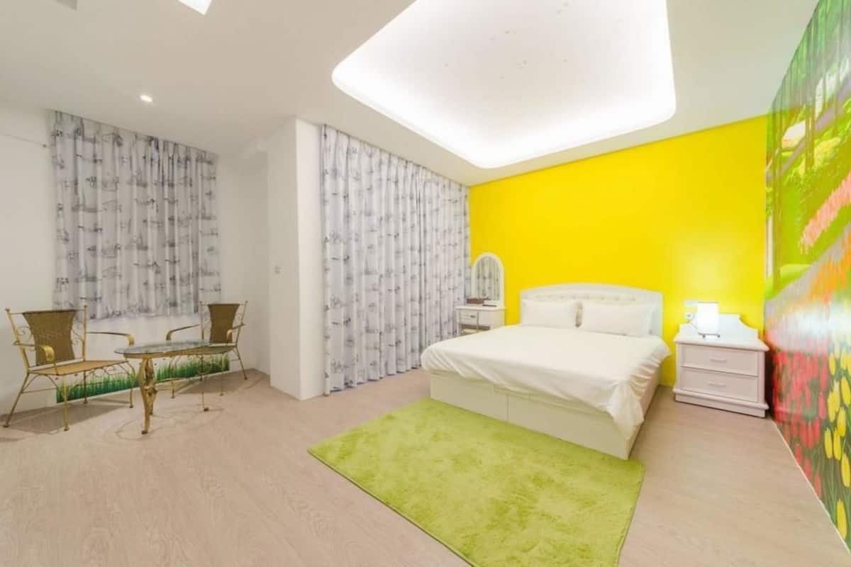 A bedroom with a bed, a nightstand, a chair, a table, and a green rug.