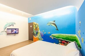 A room with a bed, a television, and a mural of dolphins and fish on the wall.