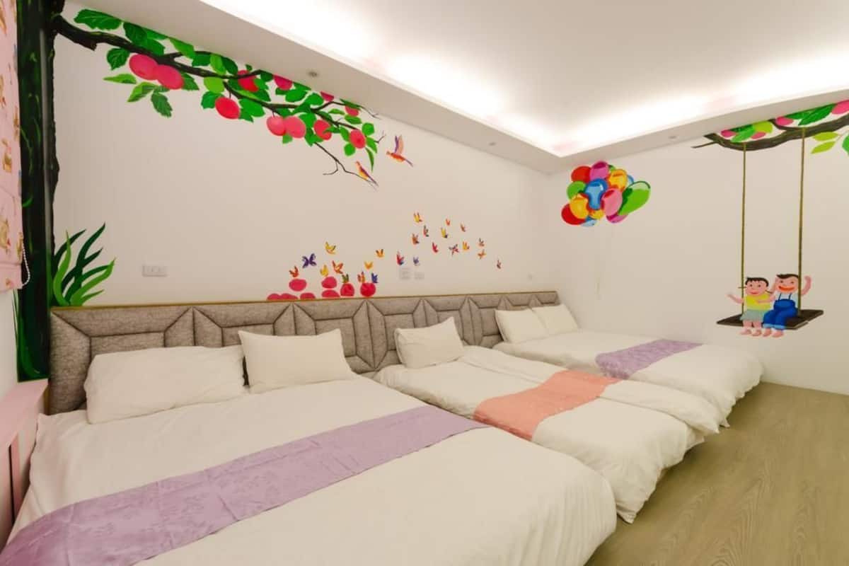 A hotel room with two beds, a headboard, and wall decorations including a tree with apples and birds.