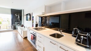 A modern kitchen with white cabinetry, a stainless steel sink, and a gas stove. - Cleo, 1BDR St Kilda Apartment (St Kilda)