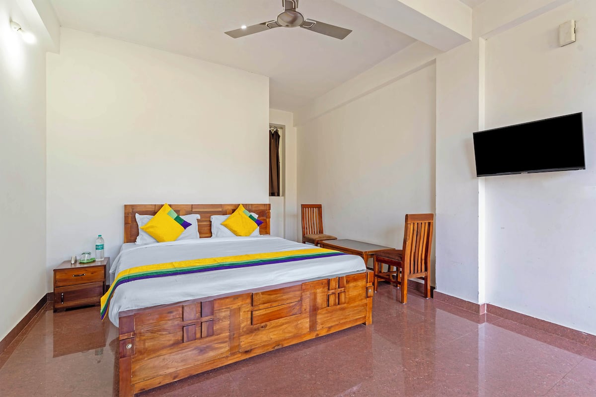 Quarto com cama de madeira, televisão na parede, escrivaninha e uma cadeira.