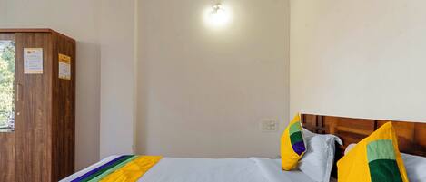 Una habitación de hotel con un armario de madera, una cama con ropa de cama blanca y almohadas de colores, e iluminación en el techo.