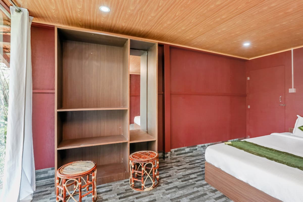 Um quarto com uma cama, um guarda-roupa, duas cadeiras de vime e uma parede vermelha.