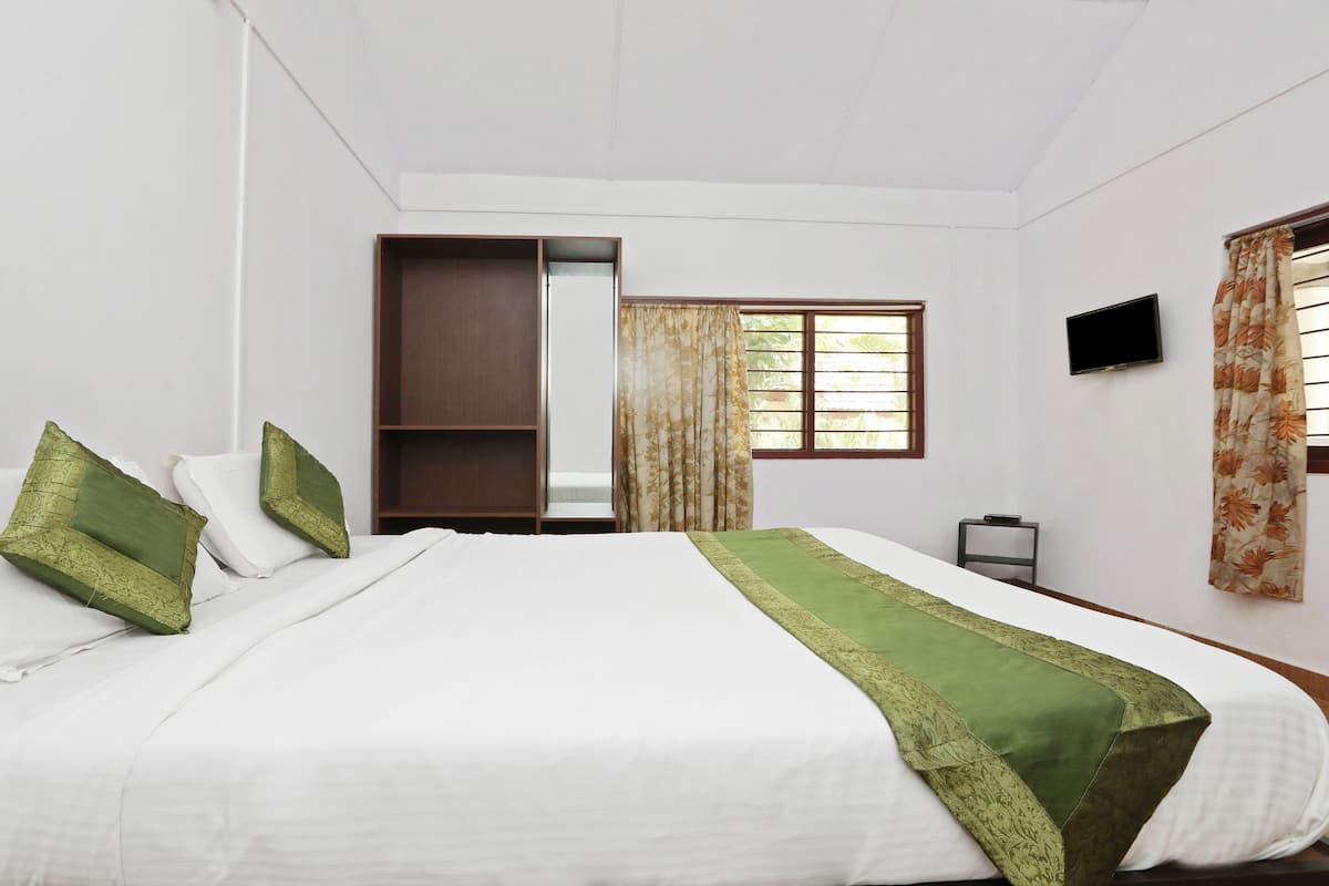 Quarto de hotel com cama, guarda-roupa, televisão e janela com cortinas.