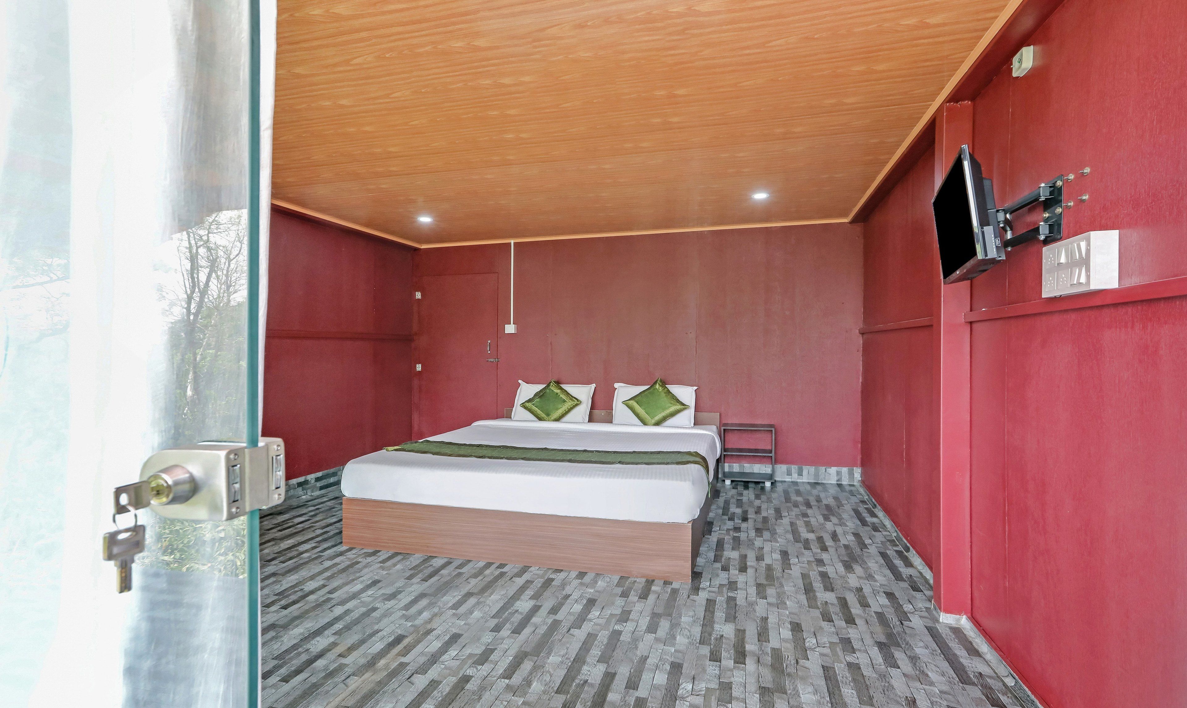 A modern bedroom with a wooden ceiling, a large bed with green pillows, and a red accent wall.