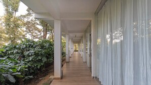 A corridor with white columns and a wooden floor, leading to a glass door. - Itsy Hotels Jammabane Cottage (Somvarpet)