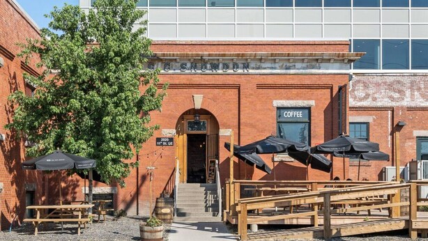 A brick building with a coffee shop sign, outdoor seating with umbrellas, and a staircase leading to the entrance. - Bright and Open Coziness. 10 minutes to Stampede (Calgary)