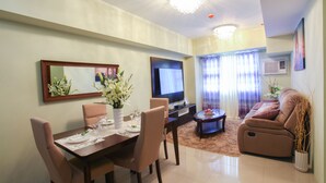 Un comedor con una mesa dispuesta para cuatro, un sofá, un televisor y un jarrón decorativo.