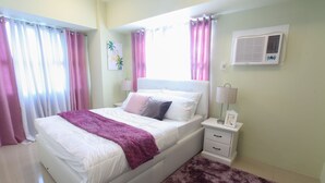 Un dormitorio con cama, mesitas de noche, lámpara, aire acondicionado de pared y cortinas.