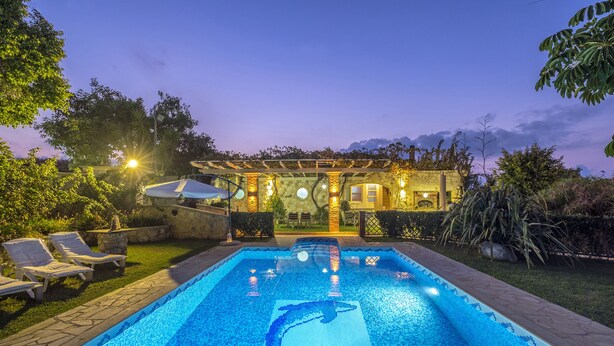 A swimming pool with a dolphin mosaic, surrounded by lounge chairs and a pergola with lights. - Niko's Art villa (Chania)
