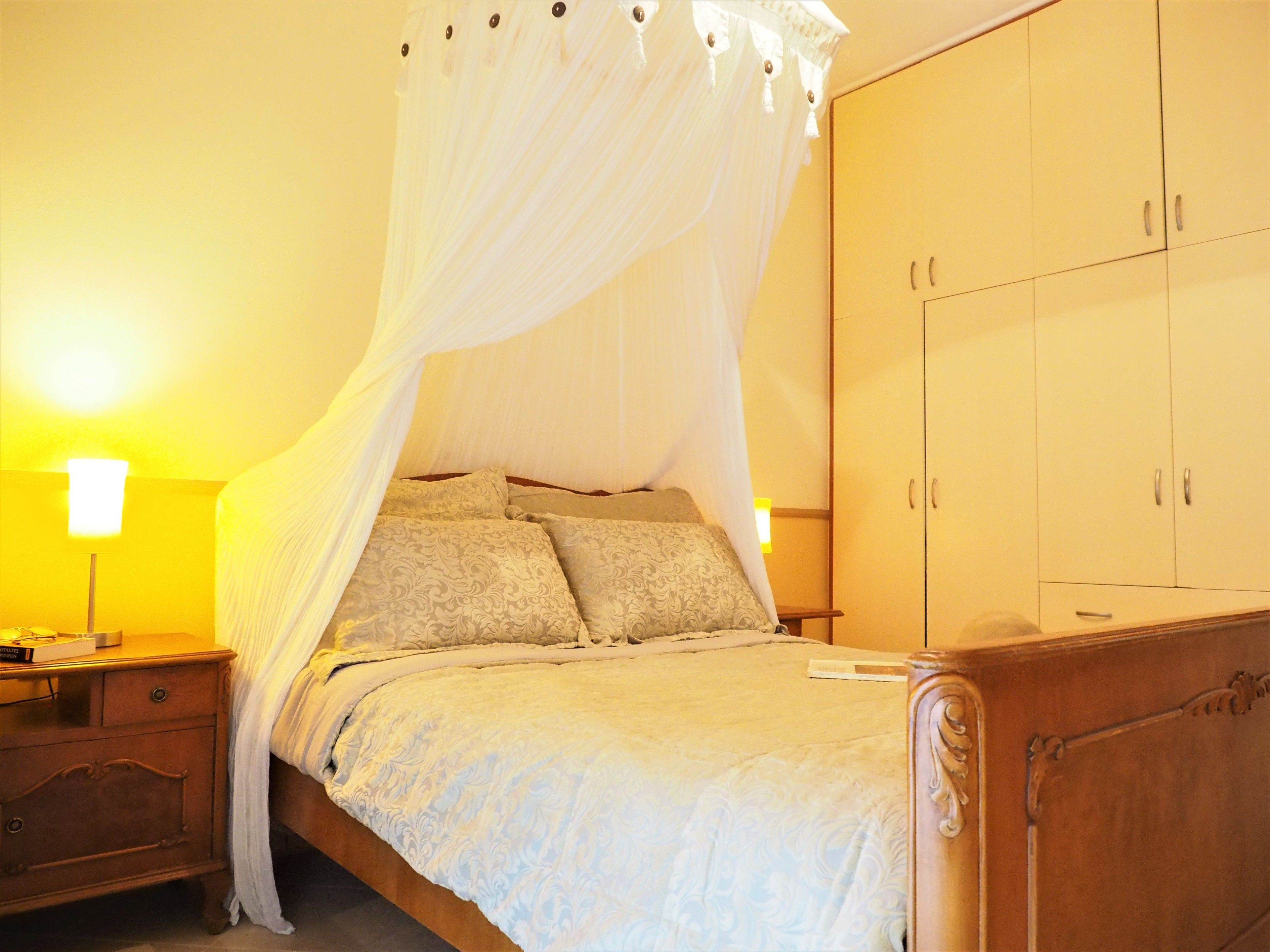 Quarto com cama de dossel, guarda-roupa de madeira, abajures e mesa de cabeceira.