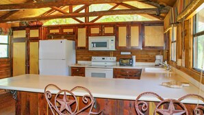 Cocina rústica de cabaña con gabinetes de madera, un refrigerador blanco, un microondas, una estufa y dos sillas con forma de estrella.