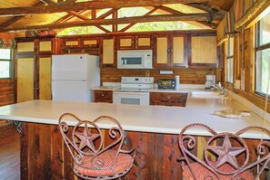 Cocina rústica de cabaña con gabinetes de madera, un refrigerador blanco, un microondas, una estufa y dos sillas con forma de estrella.