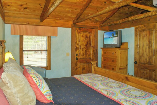 Une chambre avec un lit, une commode, un téléviseur et une fenêtre avec des stores.